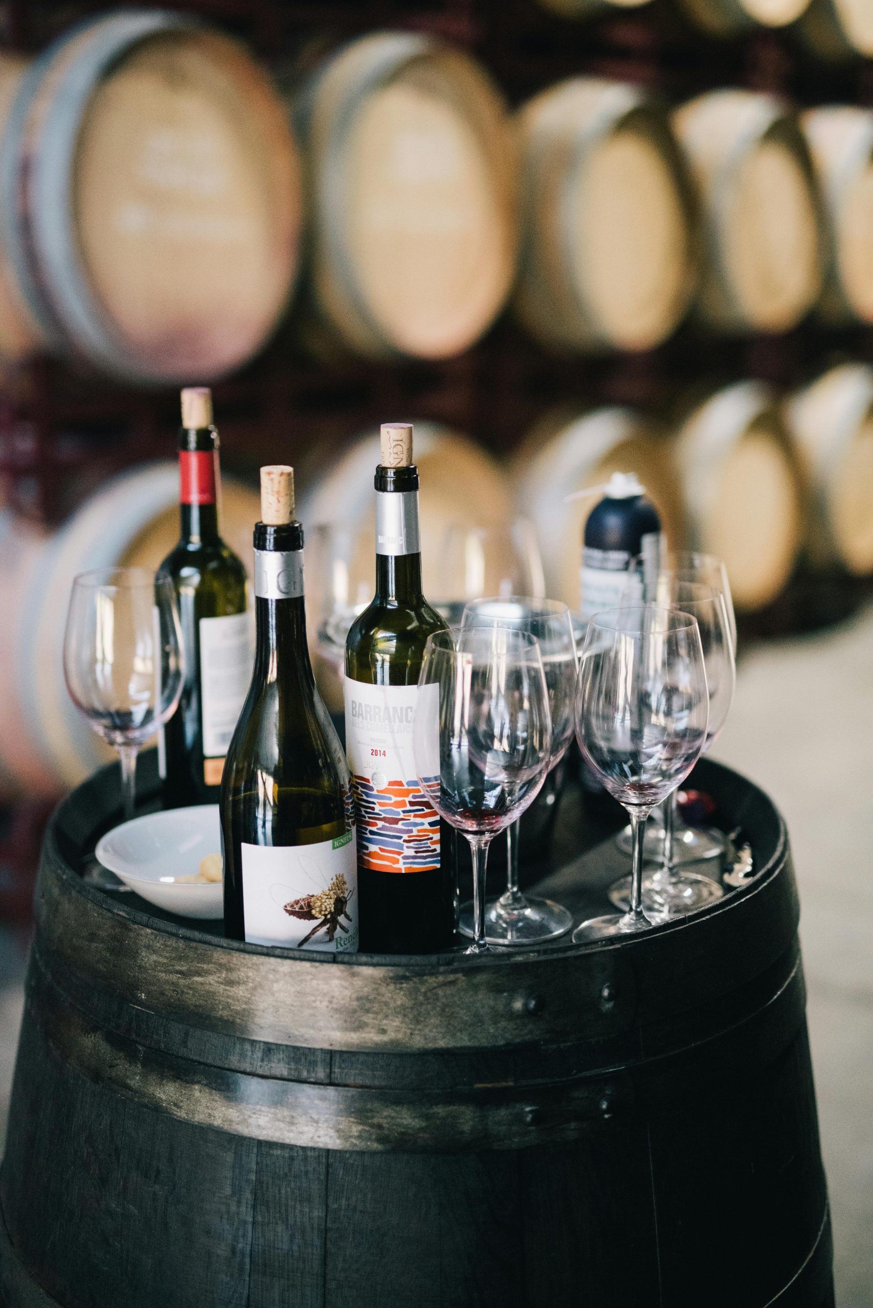 Assorted wine bottles and glasses on a barrel in a traditional winery setting.
